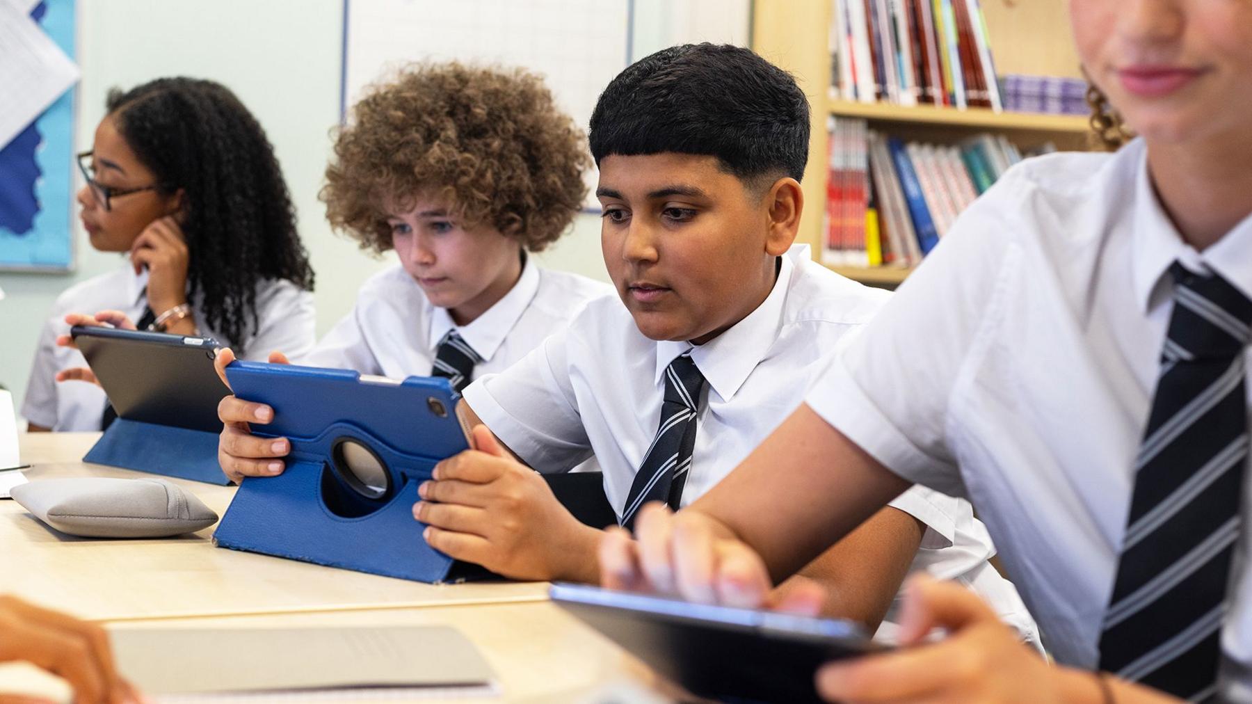 Teenage students in school uniform using touchscreen tablets in the classroom