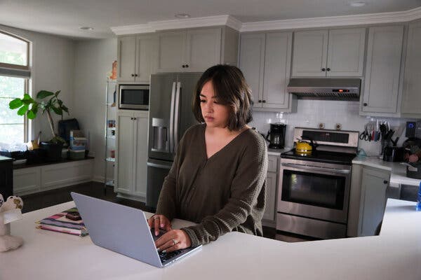Lisa Green, in a dark sweater, checking her laptop on a counter in her kitchen.