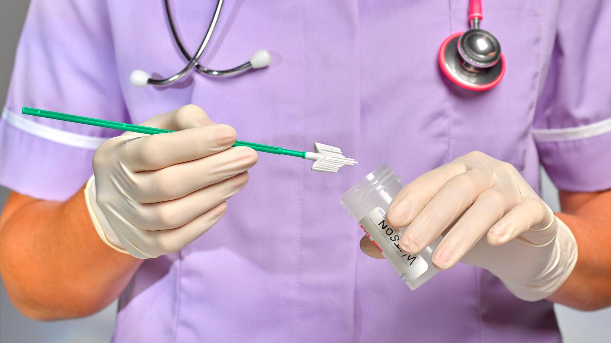 Nurse/doctor in purple scrubs holding a smear test kit.