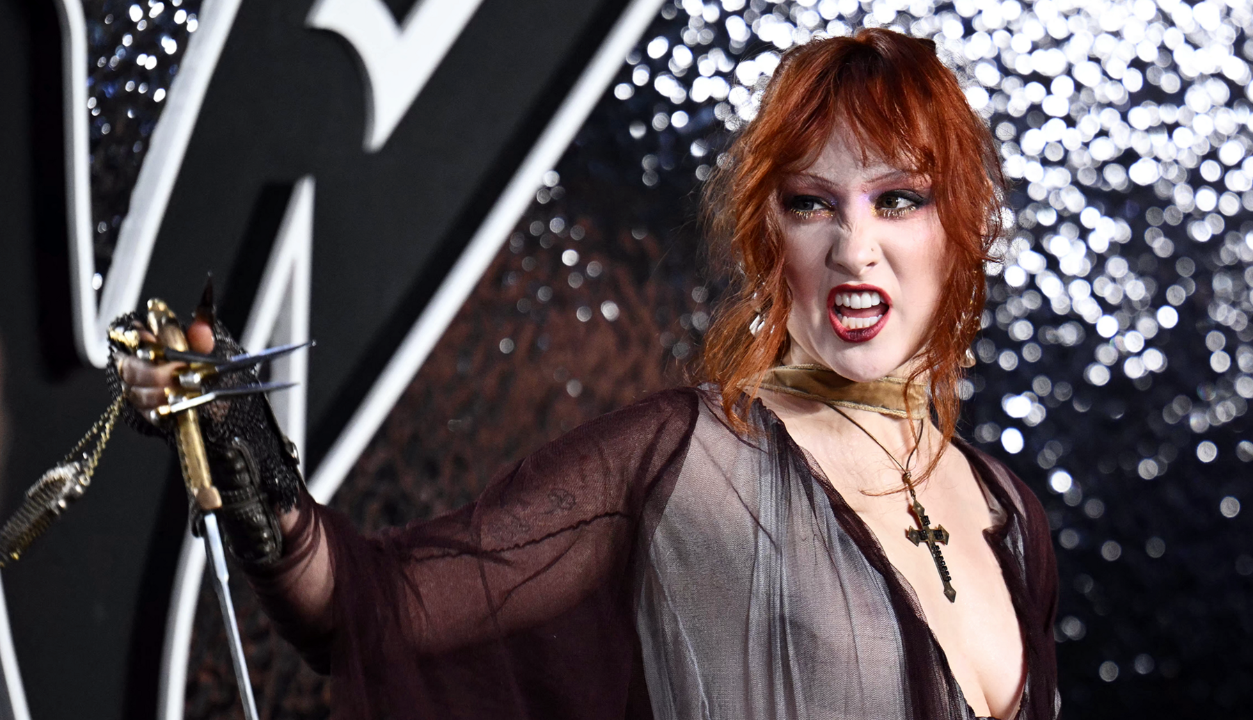 Chappell Roan snarls at the camera as she holds a fake dagger and wears a large crucifix 