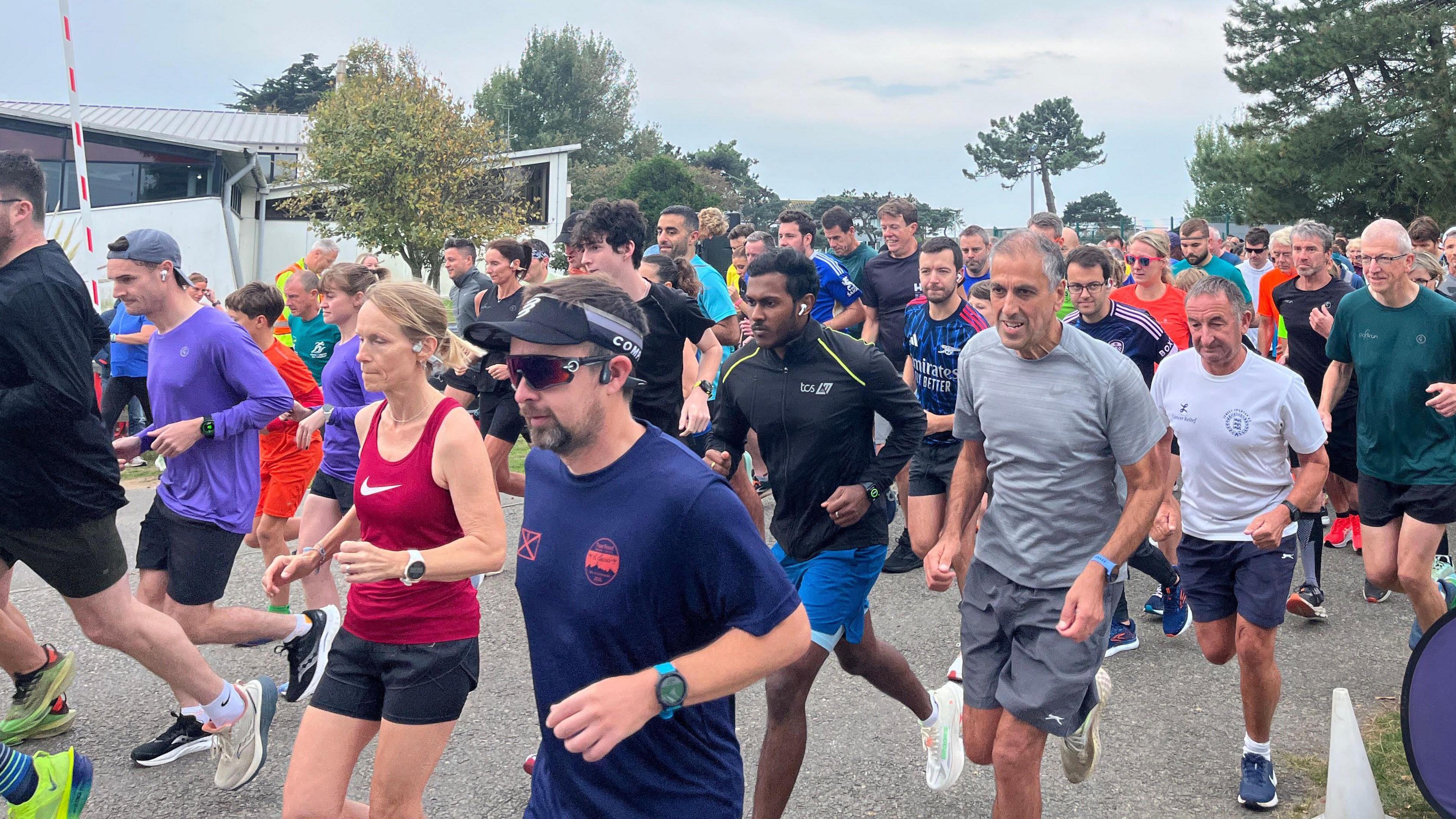 Runners are wearing brightly coloured t-shirts, and vest tops and darker running shorts as try run past the camera. There is a large group of runners filling the track.