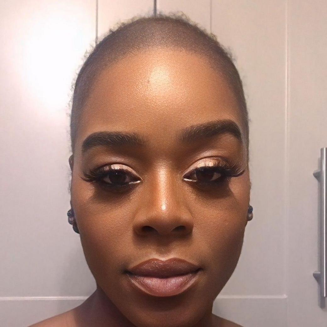 A selfie of Antonia. She is looking straight into the camera and her head is bald. She is wearing light eye shadow, lashes, and a neutral lipstick. 
