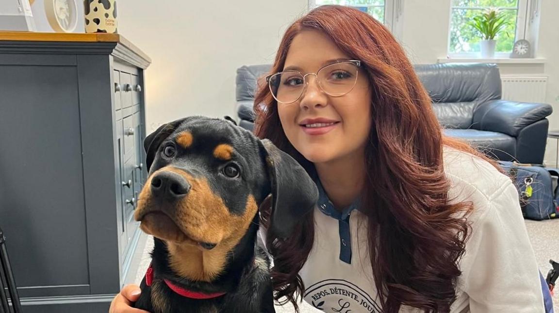 Megan is kneeling down next to a black and tan Rottweiler puppy, with her arm around him.