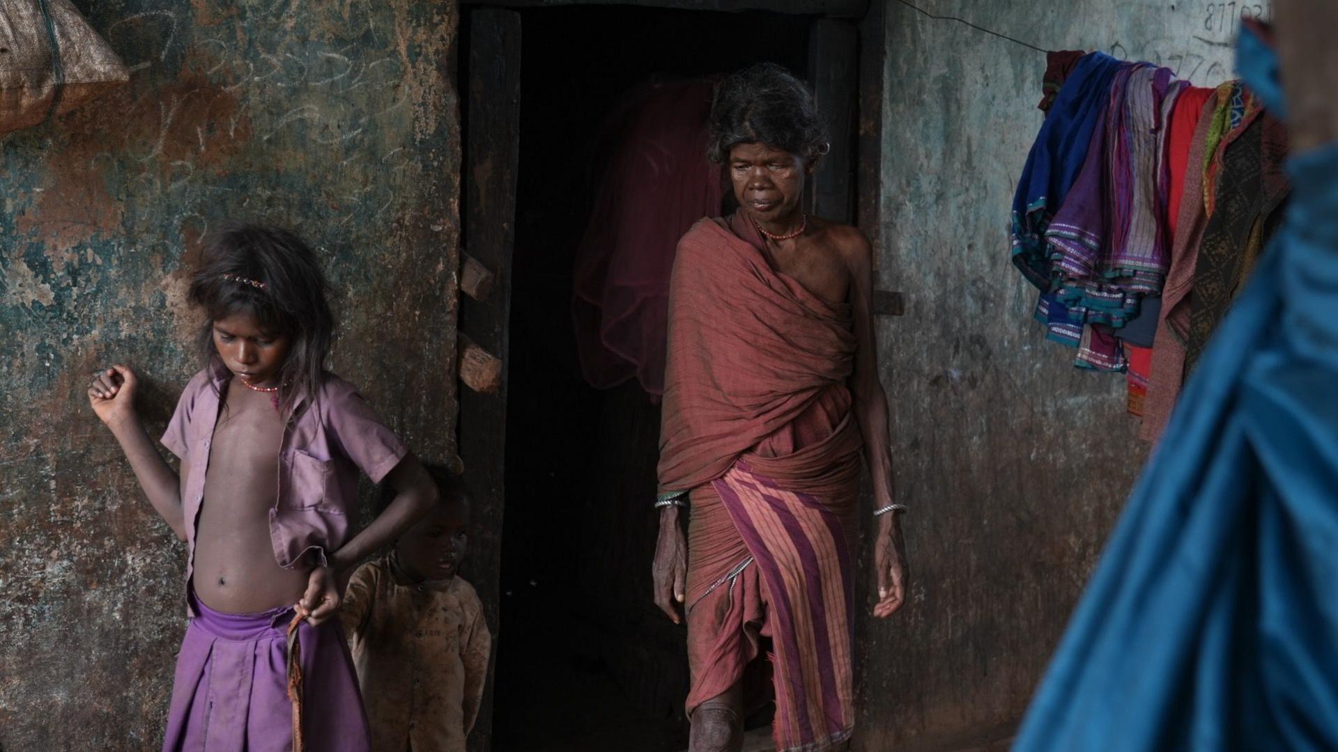 A woman and two children standing near the doorway of a dilapidated hut in a village in India's Madhya Pradesh
