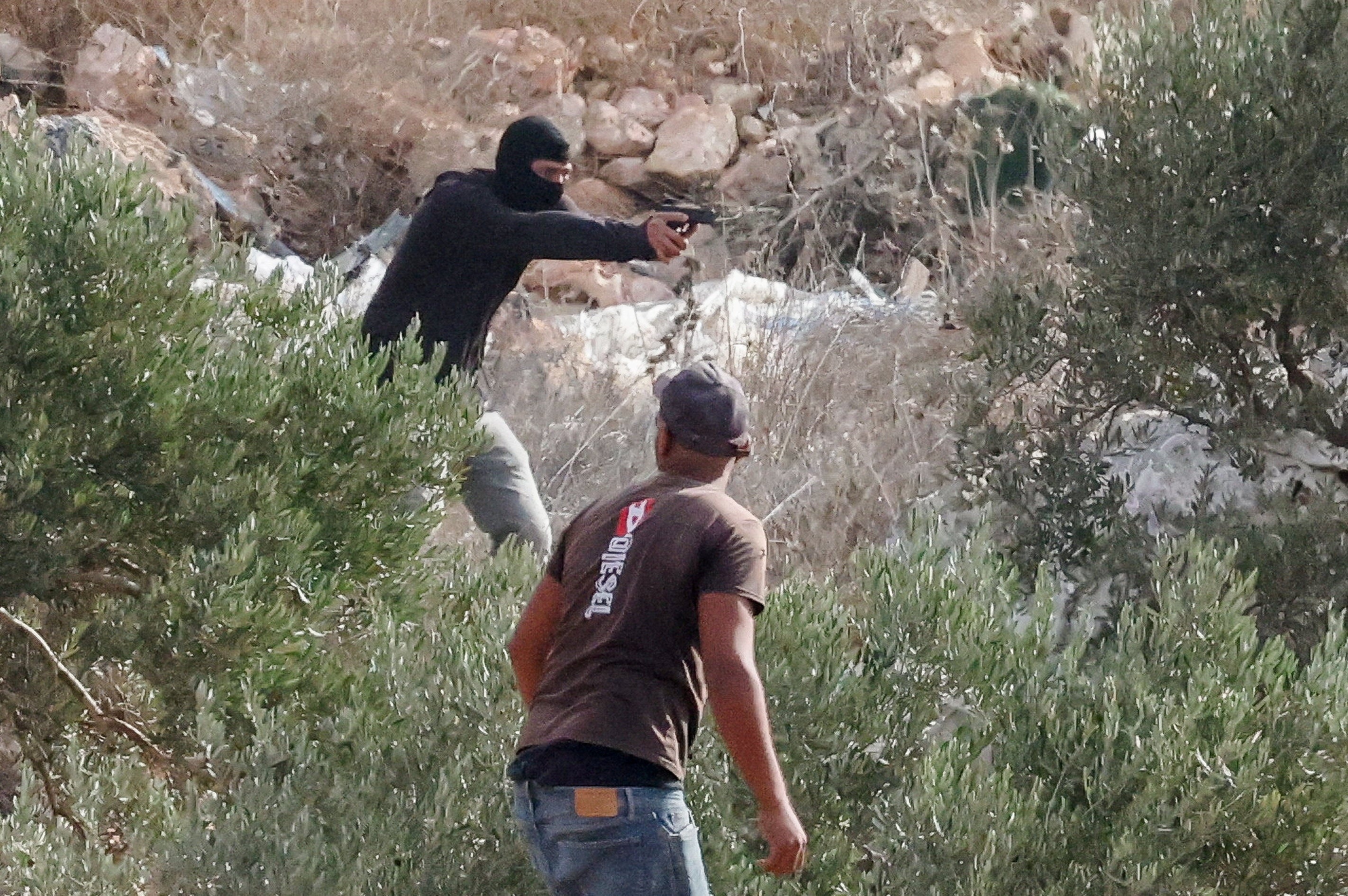 A masked Israeli points a gun as Palestinians attempt to harvest olives in Abu Falah in the Israeli-occupied West Bank, Oct. 16, 2026.