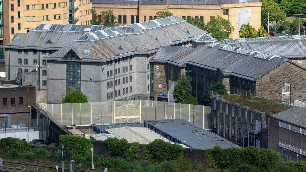 A view of HMP Cardiff, with a group of buildings in the middle of the picture, and a fence viewable from the front.
