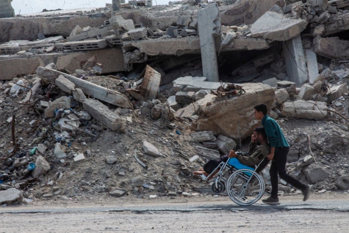 A boy pushes a man on a wheelchair past a large pile of rubble in western Gaza City, Gaza Strip, on Oct. 5, 2026.