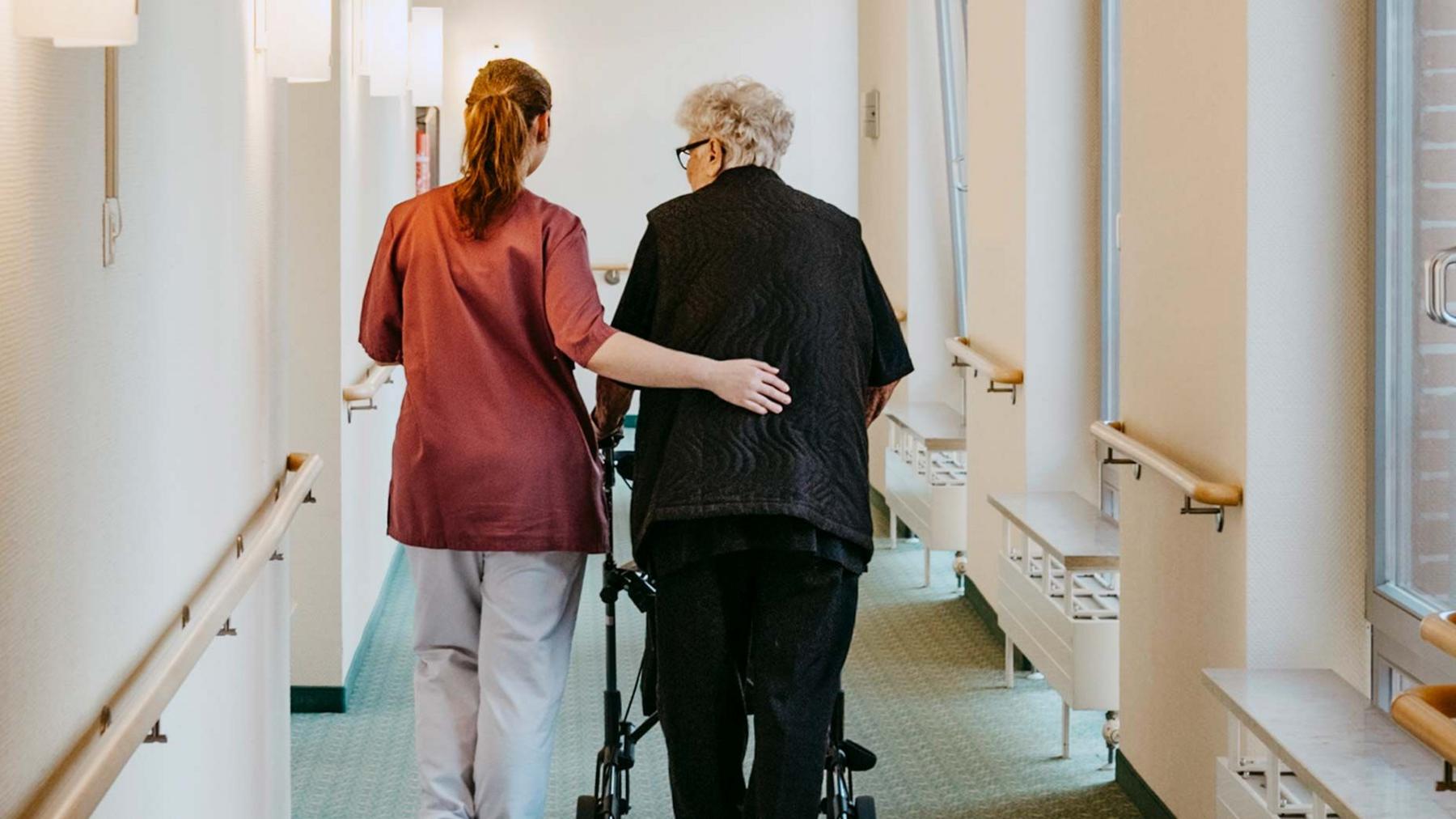 Care home staff member walking with an elderly resident