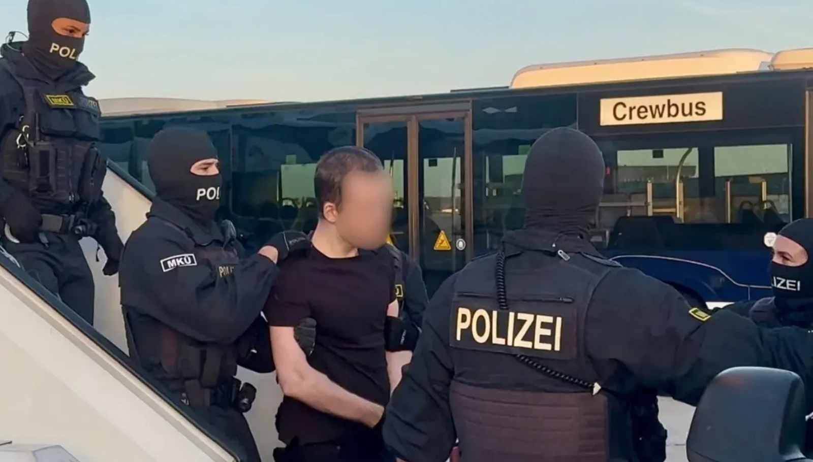 Hacker with blurred face surrounded by police. He is a skinny man in black t shirt and trousers