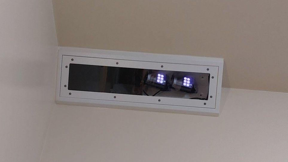 The Oxevision technology, an infrared camera, near the ceiling in the corner of a bedroom. It is in a white rectangular box and small white lights can be seen at one end. 