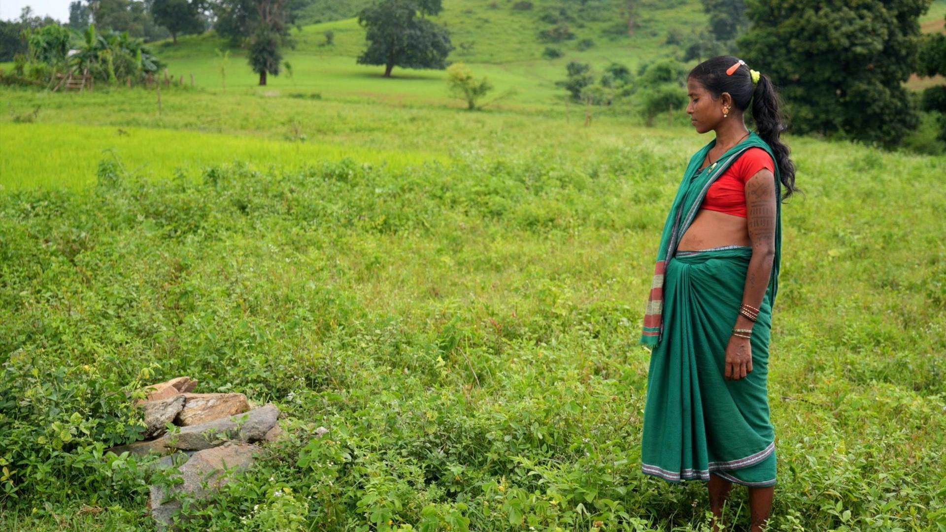 Koushila Markam, a woman wearing a green saree, looks at her daughter's grave on the ground in India's remote Matla village