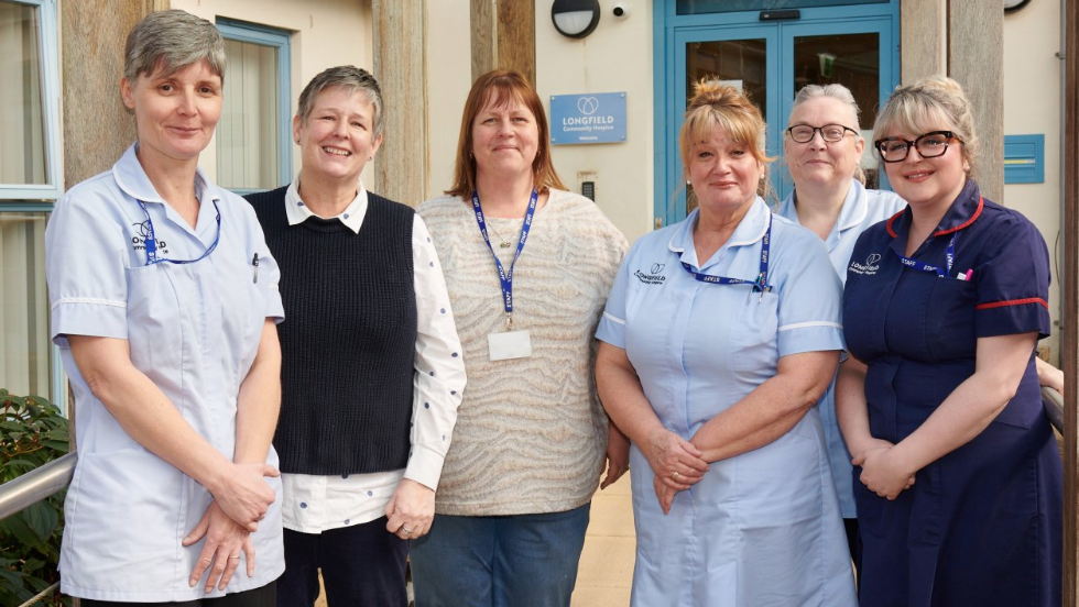 A group of women is standing together smiling at the camera, four of them are wearing nurses uniforms.